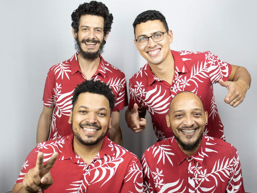 A imagem mostra os integrantes do grupo de forró “Os Quatro”. Eles usam camisetas iguais, na cor vermelha, com desenhos de folhas brancas, e sorriem animados para a câmera.