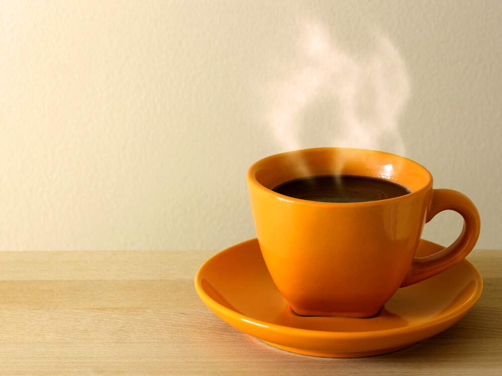 Na imagem, em uma xícara amarela com pires, há um café fumegante.