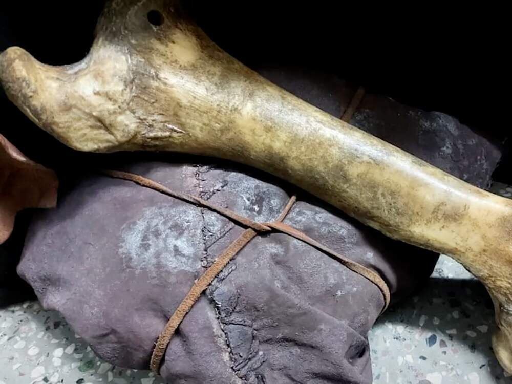 A imagem mostra um osso junto a uma embalagem pré-histórica feita de pele e cordas