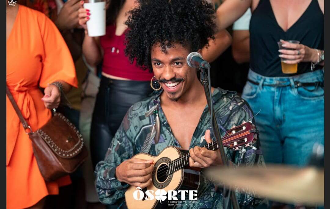 Homem negro, sorridente, tocando cavaquinho 