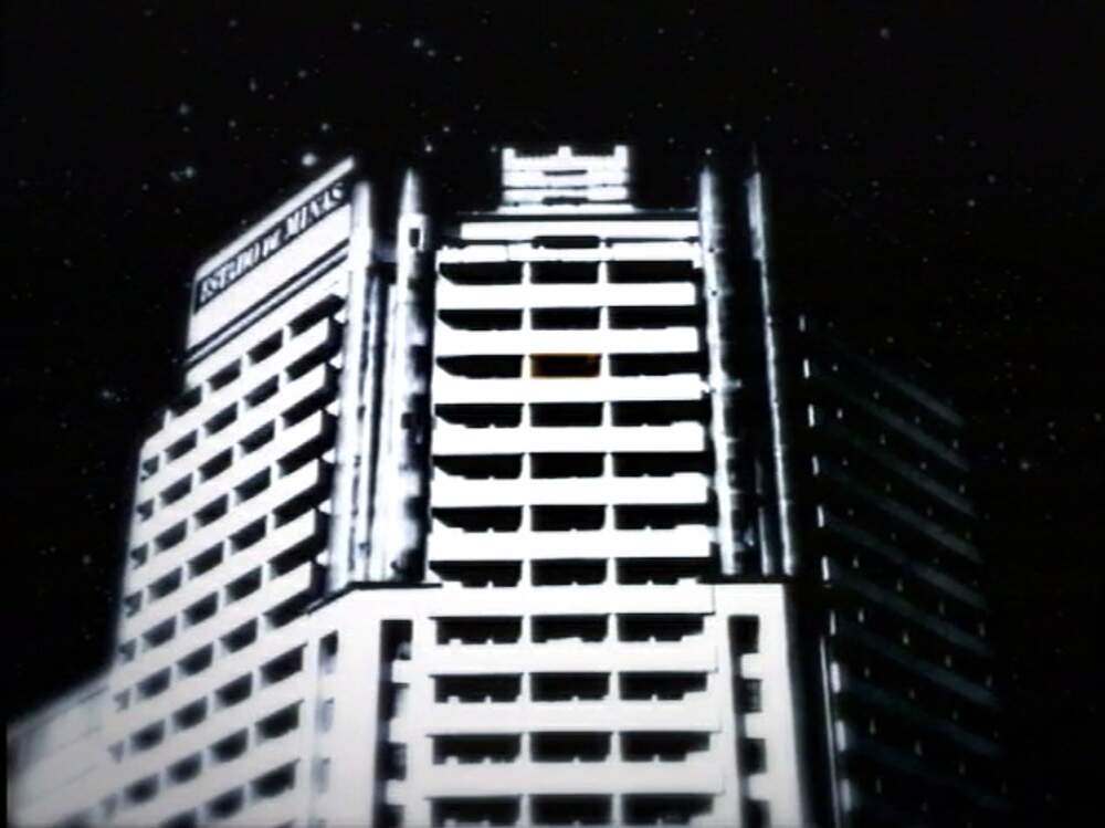A imagem mostra os andares superiores do edifício Acaiaca, em Belo Horizonte. A foto está em preto e branco e está desfocada no canto inferior esquerdo.