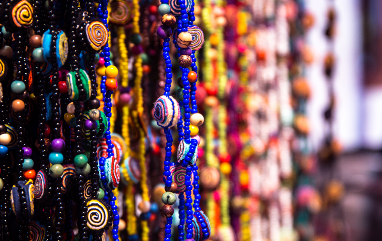 A imagem mostra vários colares de contas e cordão dependurados, são de varias cores.