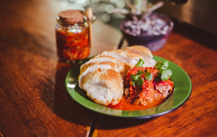 Foto de um prato com Carne suã mineira ao molho de tomate. Acompanhado de pão de sal.