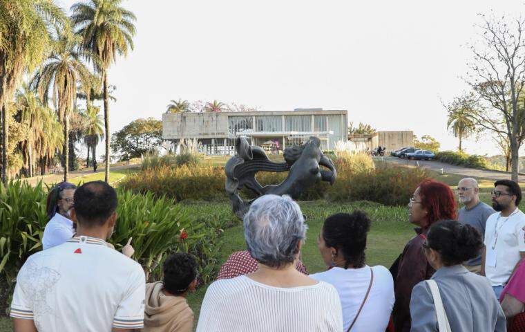 Grupo de pessoas admira os jardins do Museu de Arte da Pampulha. Elas estão de costas para a câmera olhando de frente ao Museu