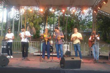 Seis homens com instrumentos nas mãos. Eles estão encima de um palco. 