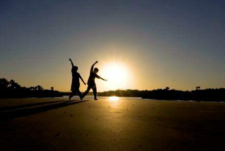 A imagem mostra a silhueta de dois bailarinos contra a luz do por do sol na pampulha