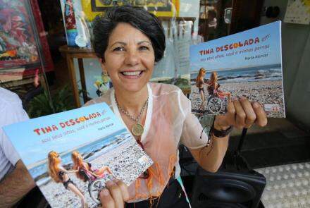 Marta Alencar, criadora da personagem cadeirante Tina Descolada, segurando seu livro sobre histórias da Tina