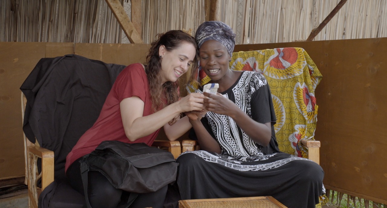A imagem mostra as duas amigas, Joana e Kevin, sentadas em um sofá e vendo algo no celular
