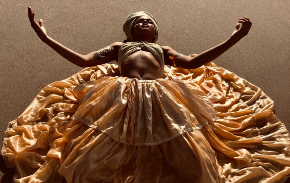 Na imagem, uma mulher negra deitada com um turbante e uma saia.