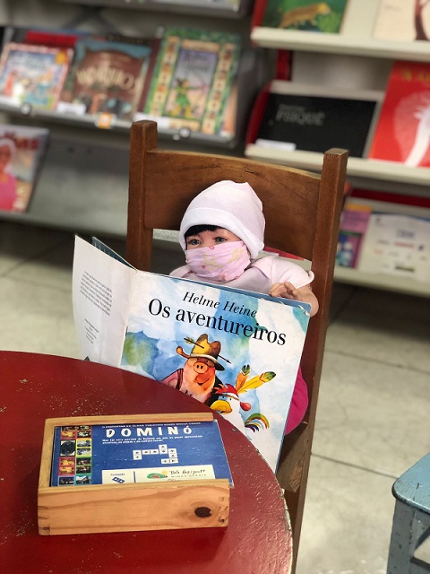 Boneca de mascara segurando um livro infantil