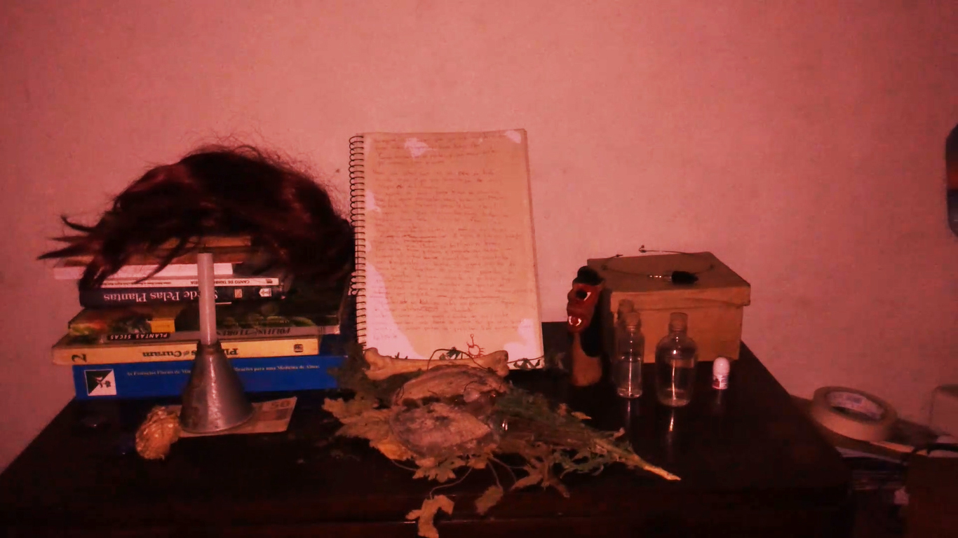 fotografia de divulgação do filme "Para todas as moças". Na cena com aspécto de foto antiga, objetos como um caderno, uma vela, livros estão em cima de uma mesa.