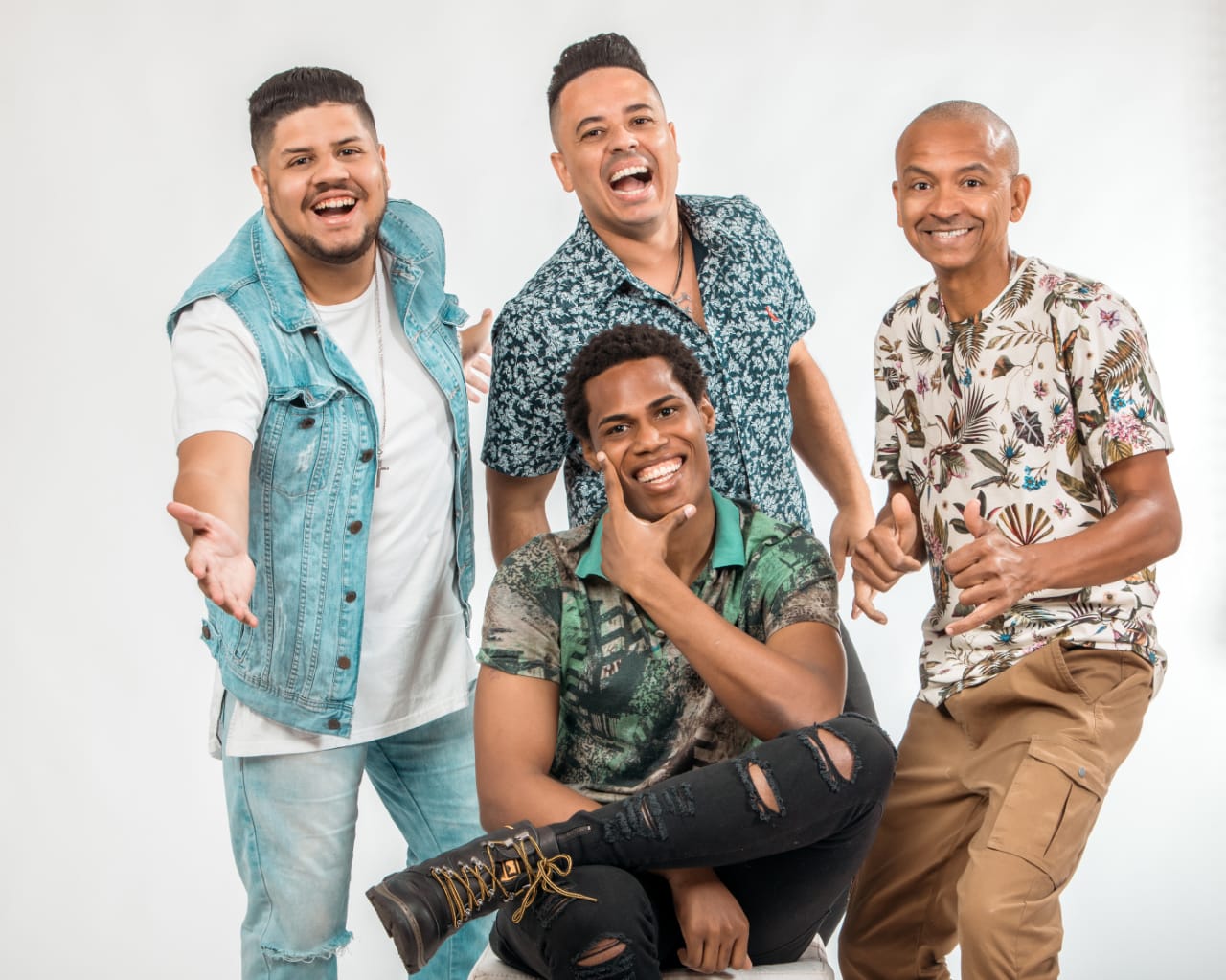Foto com fundo branco, em destaque, a banda Magnatas do Samba, composta por quatro homens, um deles sentado.