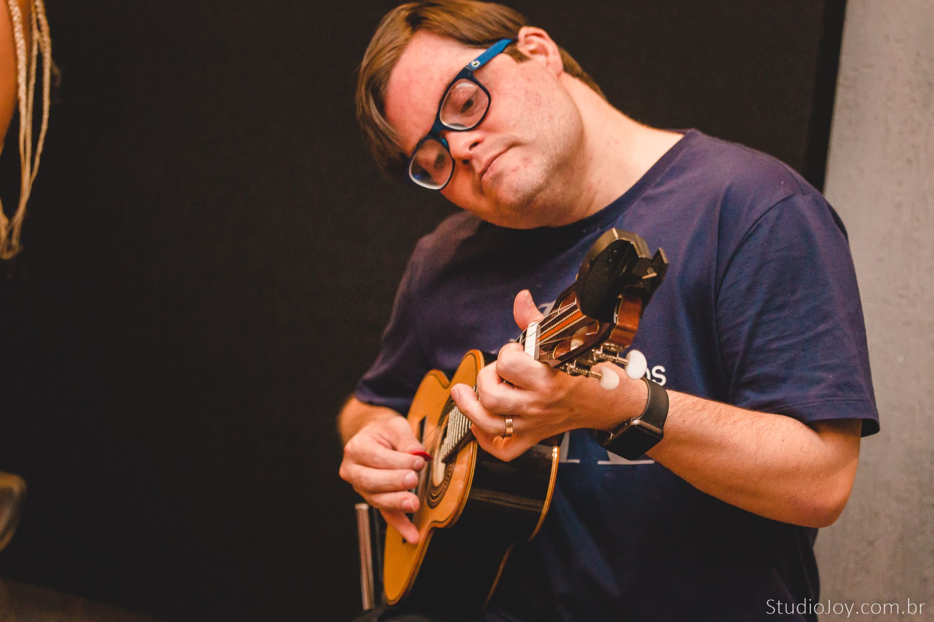 Foto com o Dudu, um homem branco, com óculos, vestindo uma camisa azul, tocando um cavaco.