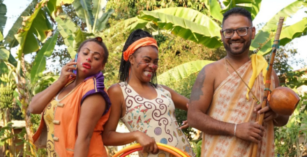 Três pessoas negras com cara pintada, roupas coloridas e instrumentos.