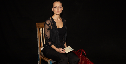 Foto de Chica Portugal sentada em uma cadeira com uma carta na mão. 