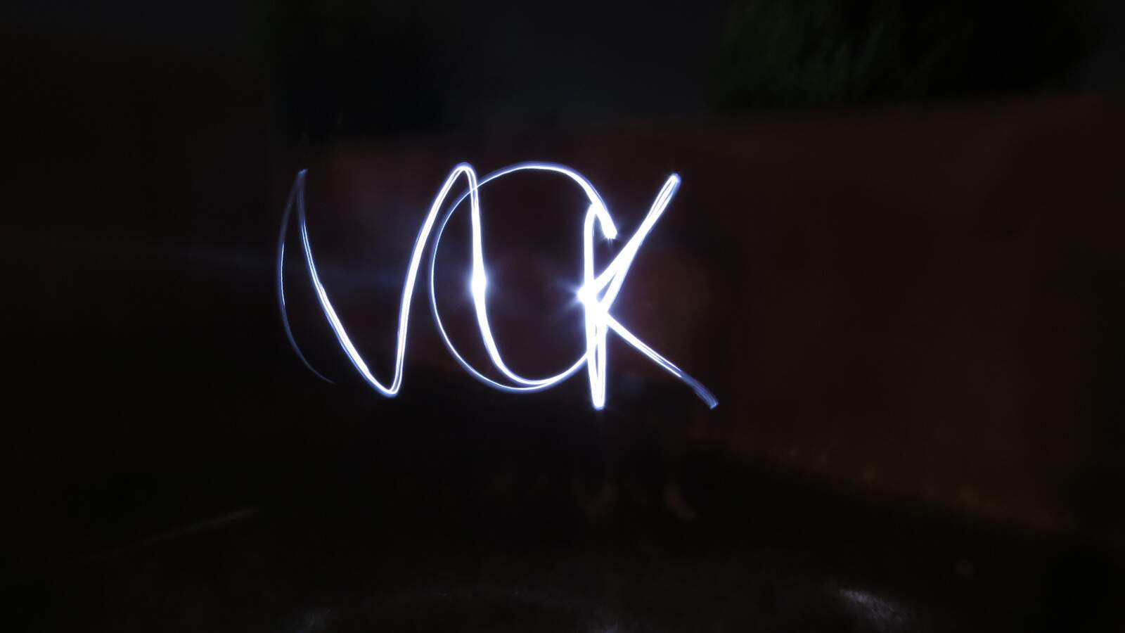 Fundo preto com o escrito MCK em evidencia. A sigla a luz foi captada pela técnica da luz em movimento por meio de uma longa exposição fotográfica