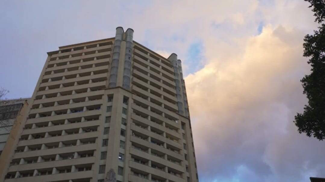 Imagem mostra o Edifício Acaiaca. A fotografia foi tirada debaixo para cima permitindo ver boa parte do prédio e o céu azul com nuvens