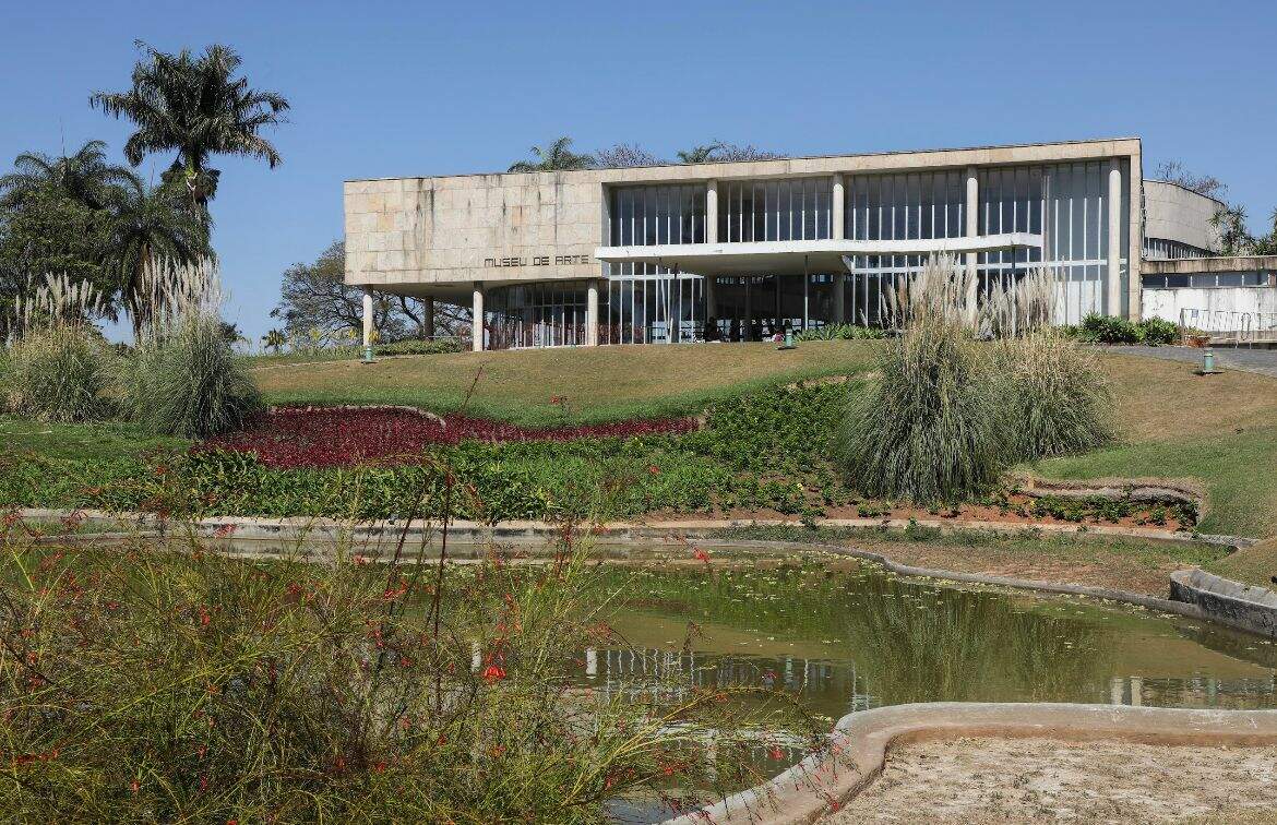 A imagem mostra a fachada do Museu de Arte da Pampulha. É possível observar os jardins do espaço, com o lago, gramado, e ávores