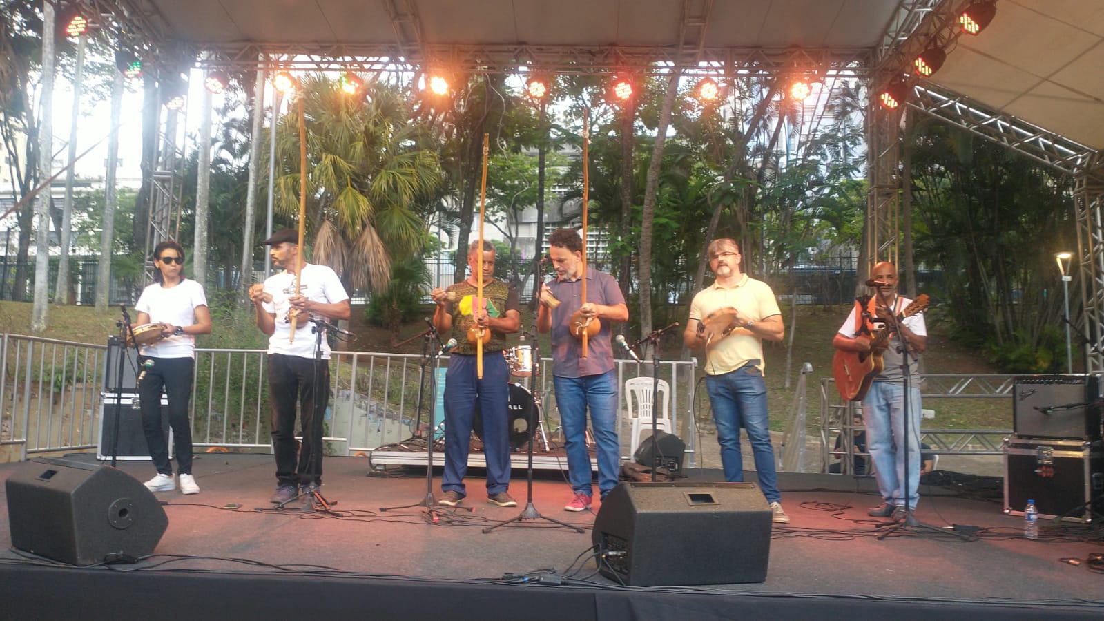 Seis homens com instrumentos nas mãos. Eles estão encima de um palco. 