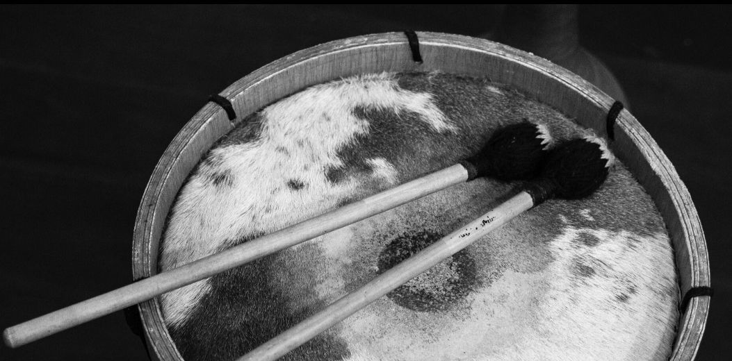 Imagem em preto e branco apresenta um tambor e duas baquetas. O registro mostra o instrumento de cima para baixo