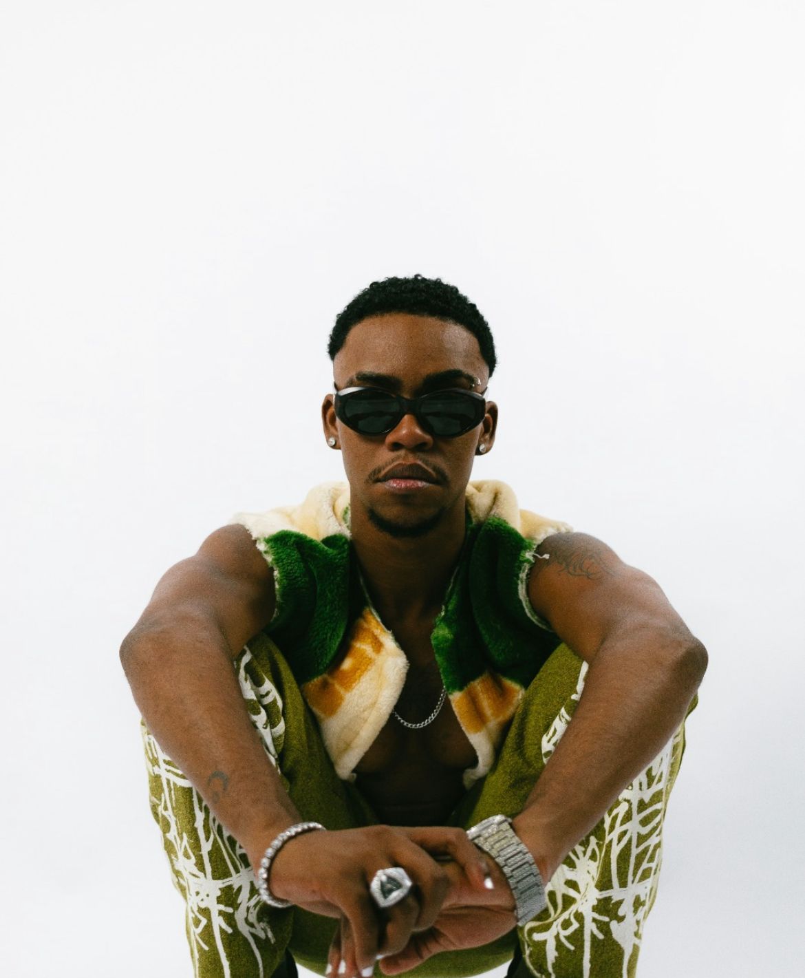 Akin Zahin em Soul Ritmo & Melodia (Foto: Divulgação) Homem negro agachado, com as mãos cruzadas. Ele usa óculos escuros, roupa colorida, anéis e pulseiras prateadas