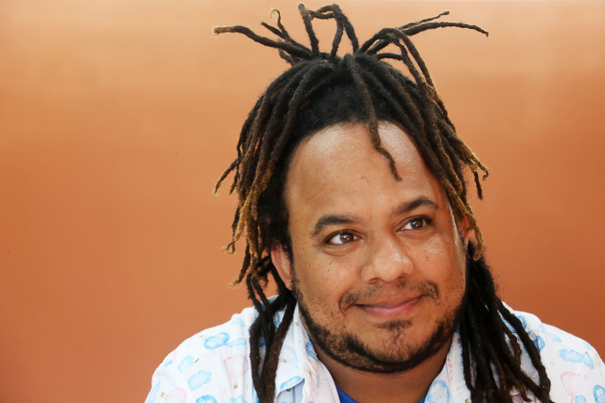 Élcio Paraíso Homem negro, com cabelos trançados e presos, sorrindo discretamente.