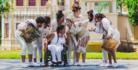 Fotografia de um grupo de palhaços se entreolhando. Eles vestem roupas claras ou brancas e estão com pinturas brancas no rosto e nariz vermelho