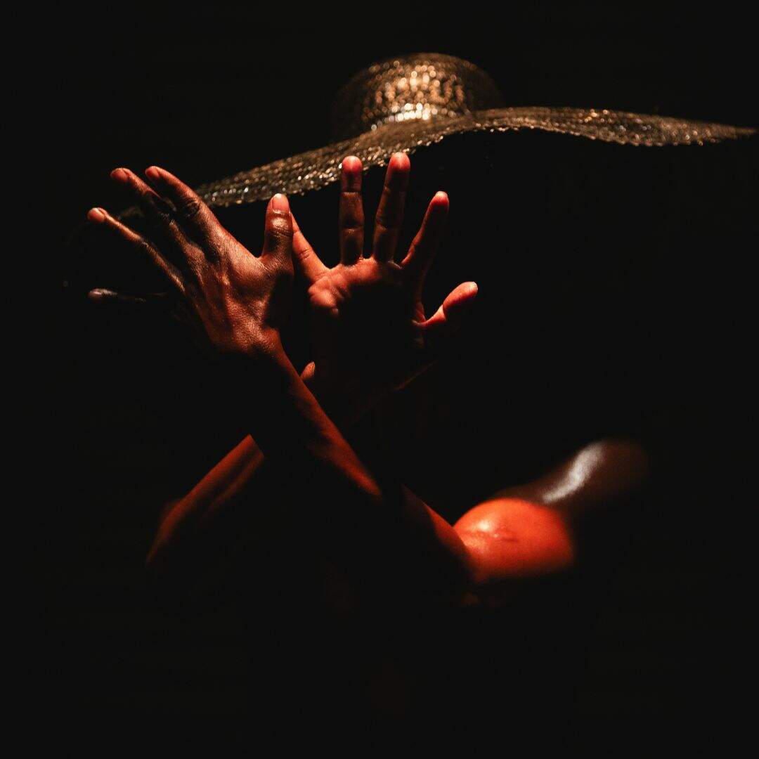 Na imagem, um homem negro usa um chapéu enquanto suas mãos repousam uma sobre a outra, com a ponta de uma sobreposta à outra.