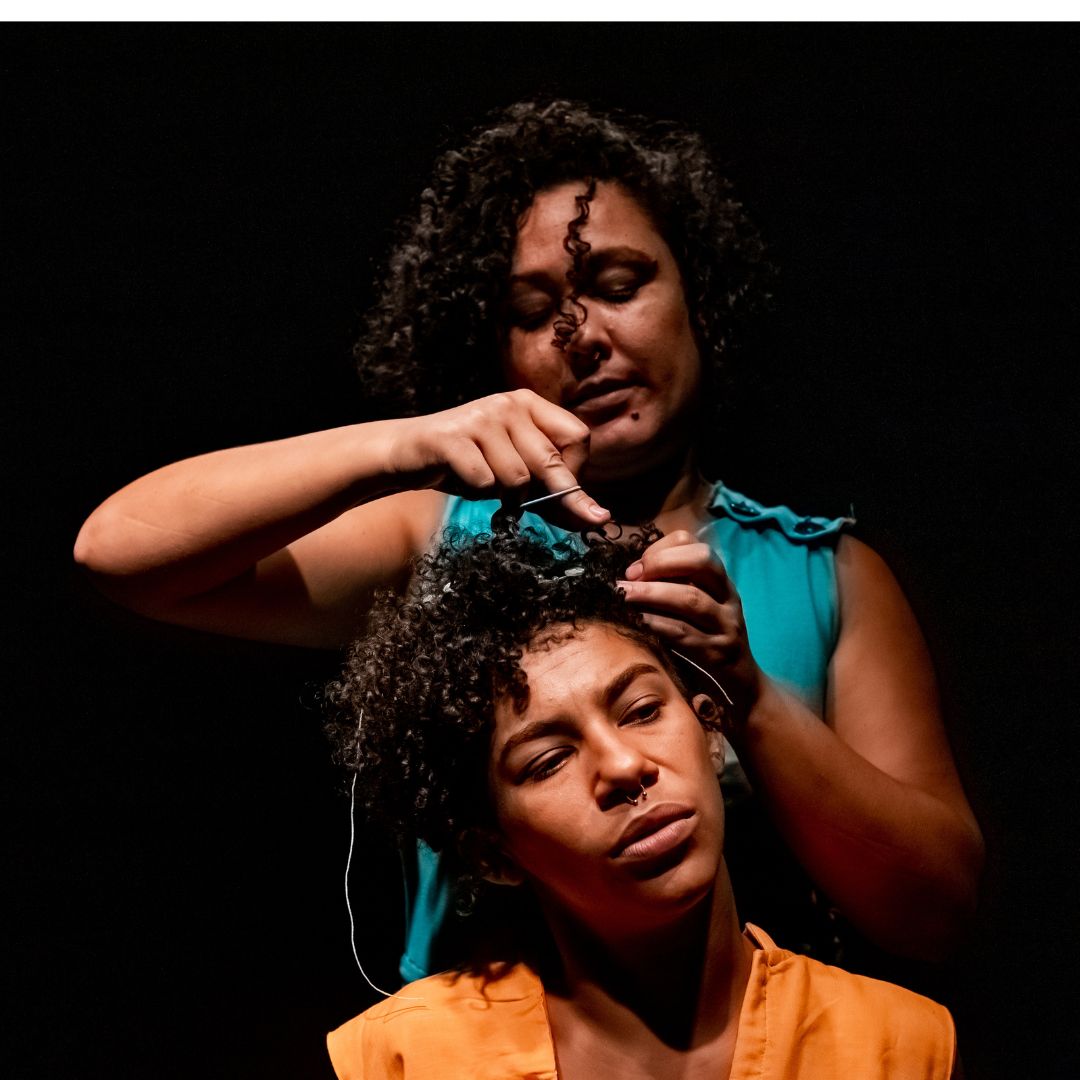 Duas mulheres: uma sentada, a outra em pé arrumando seu cabelo.