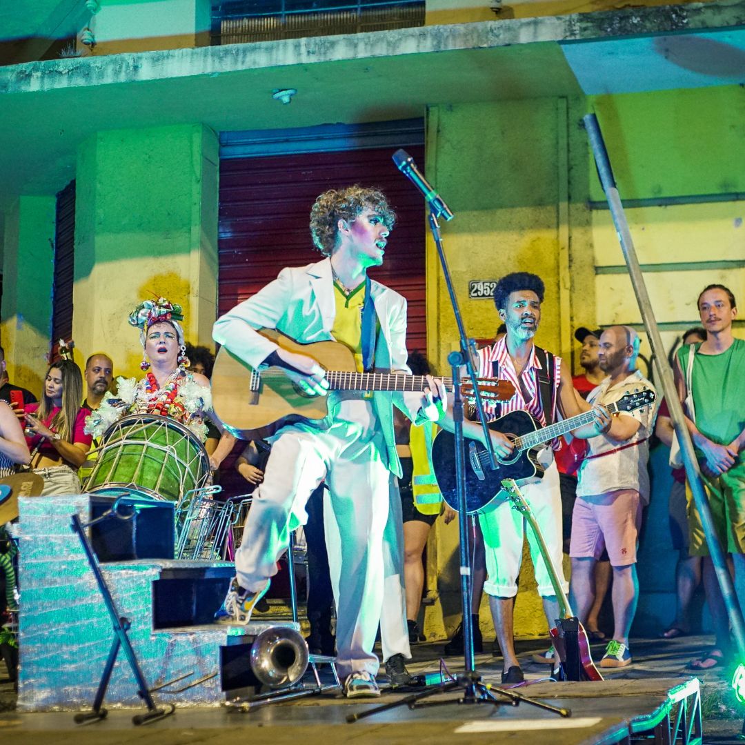 um homem branco, canta com um violão em volta de um público 