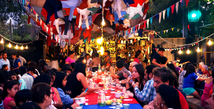 Na foto, pessoas compartilham comidas em uma mesa comunitária