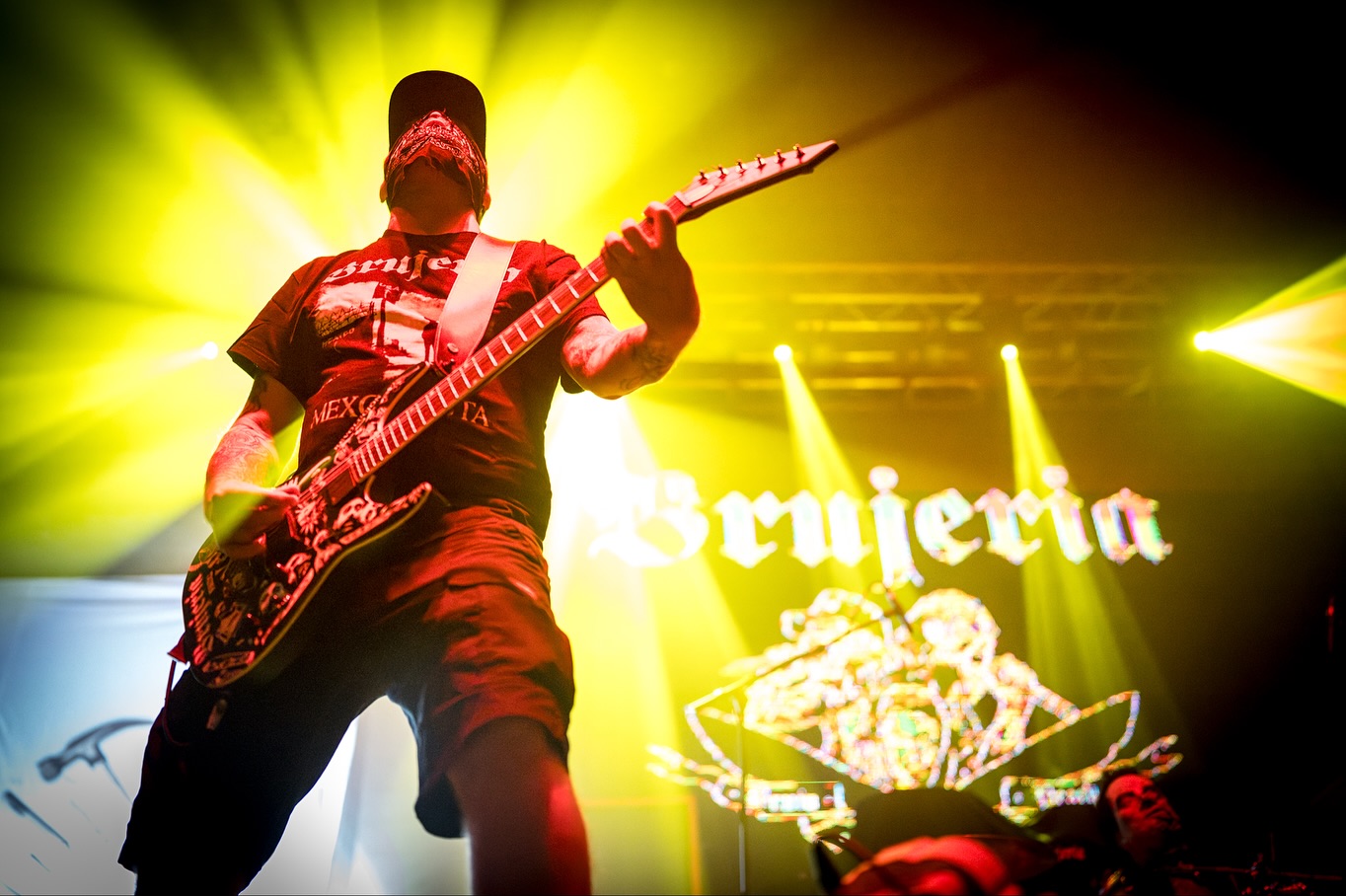 homem com roupa preta, segurando uma guitarra com luz amarela no fundo 