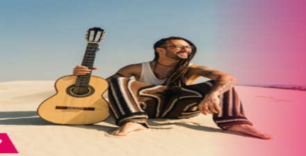 Foto mostra um homem sentado na praia segurando um violão
