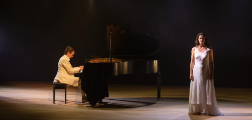 Imagem de um homem tocando piano e uma mulher em pé ao lado com o vestido branco