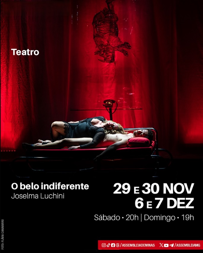 Espetáculo: "O Belo Indiferente" - Cena teatral iluminada por luz vermelha intensa. Uma mulher está deitada sobre um homem em uma cama metálica, em um momento de forte carga dramática. Ao fundo, cortinas vermelhas e uma escultura pendurada compõem o cenário.