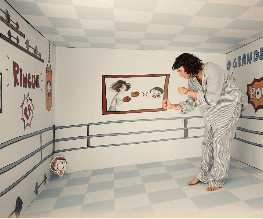 Imagem de uma mulher em um quarto desenhado, com um desenho de uma criança, simulando uma "luta"