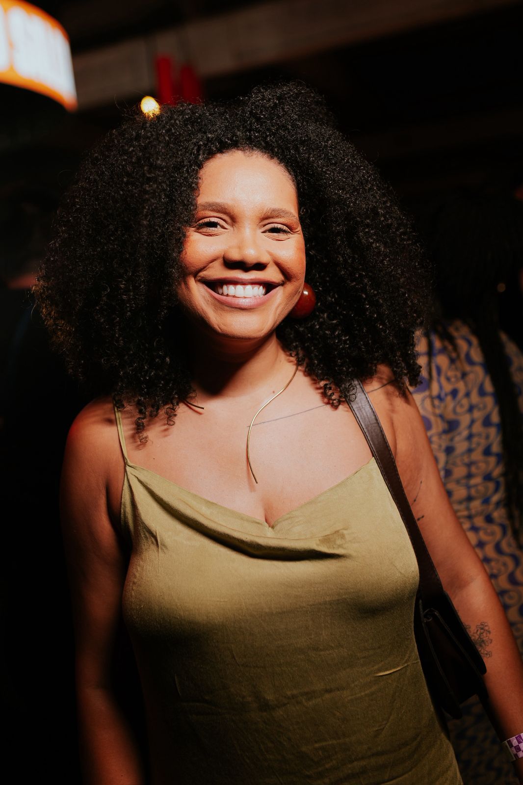 Uma mulher preta cis de cabelo cacheado volumoso com um vestido verde musgo