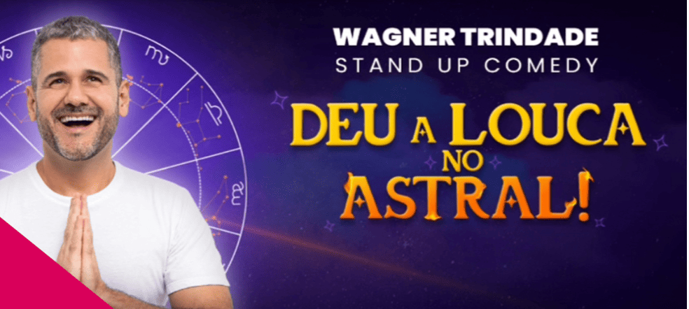 Banner promocional do show de stand-up de **Wagner Trindade**, intitulado **"Deu a Louca no Astral!"**. O humorista aparece à esquerda, sorridente e com as mãos postas em sinal de agradecimento, sobreposto a um fundo roxo com um mapa astral e constelações. O título do show ganha destaque à direita em letras amarelas e laranjas com brilhos, reforçando a temática mística e divertida da apresentação.