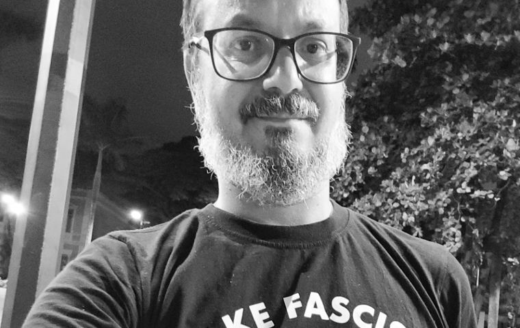 Uma selfie com um homem em pé, vestido de blusa preta com o desenho de uma caveira escrito make facists. Está à noite e ele está na rua. 