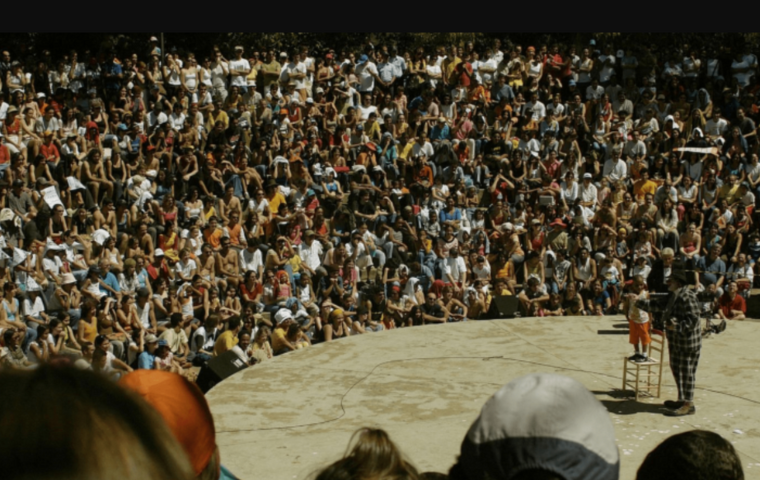 Imagem de edições anteriores do FIT BH, com uma apresentação de um palhaço num picadeiro e em volta o público sentado assistindo lotando a platéia.