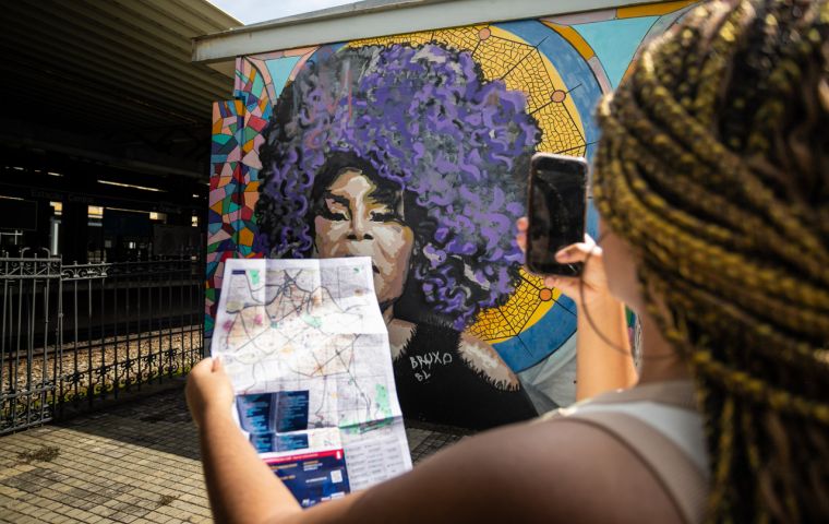 Foto: Alice Guimarães / Acervo Belotur Garota tirando foto de mural, segurando o mapa da região central de BH