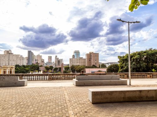 O mirante da Rua Sapucaí em um dia claro. O piso é de blocos de pedra retangulares. Há grandes bancos de concreto dispostos no local. Ao fundo, o gradil de cimento da mureta e, abaixo, a vista do centro da cidade, com o Viaduto de Santa Tereza e muitos prédios sob um céu com nuvens.