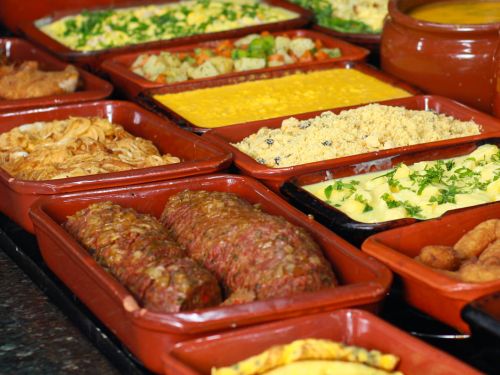 Foto do self service do restaurante contendo linguiça, pure de batata, farofa e outros pratos 