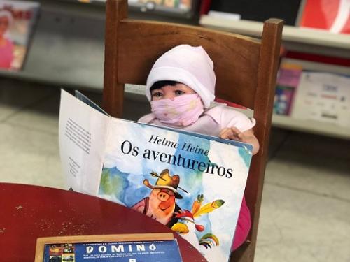 Boneca de mascara segurando um livro infantil