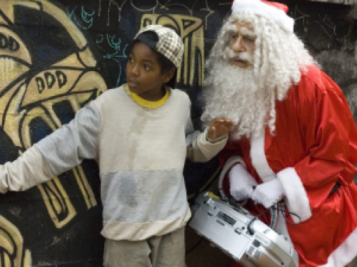 Foto com uma criança atenta, encostada na parede, com o Papai Noel, segurando uma maleta.
