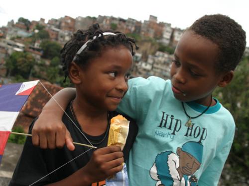Foto com duas crianças se abraçando, uma delas com um picolé em mãos.