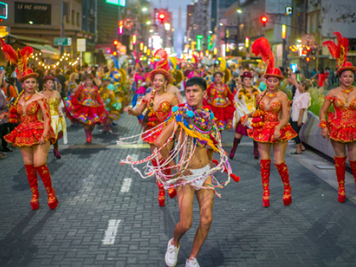 Foto de atores na rua vestidos com roupas chamativas, como em um cortejo de carnvaval. 