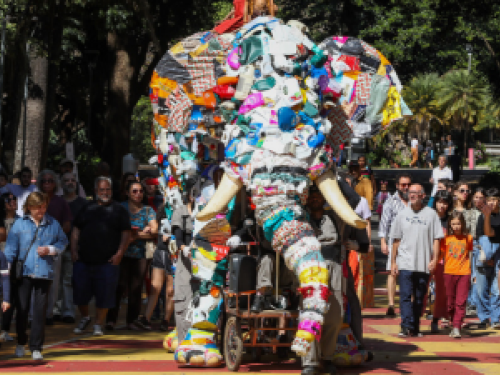 Um Elefante gigante feito de materiais recicláveis e manipulado por atores anda pelas ruas da cidade