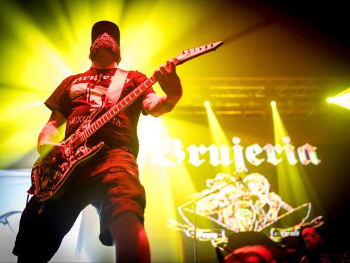 homem com roupa preta, segurando uma guitarra com luz amarela no fundo 