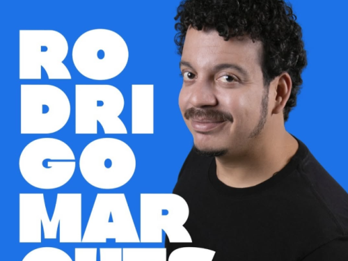 Imagem azul com um homem de blusa preta, barba e cabelos cacheados 